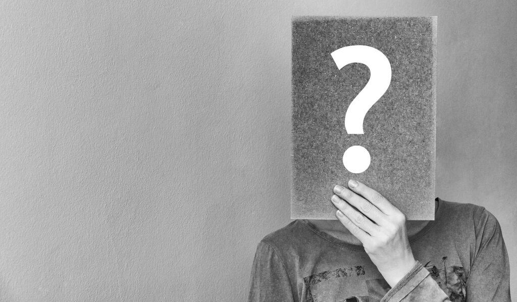 black and white photo of a woman holding a question mark that covers her face